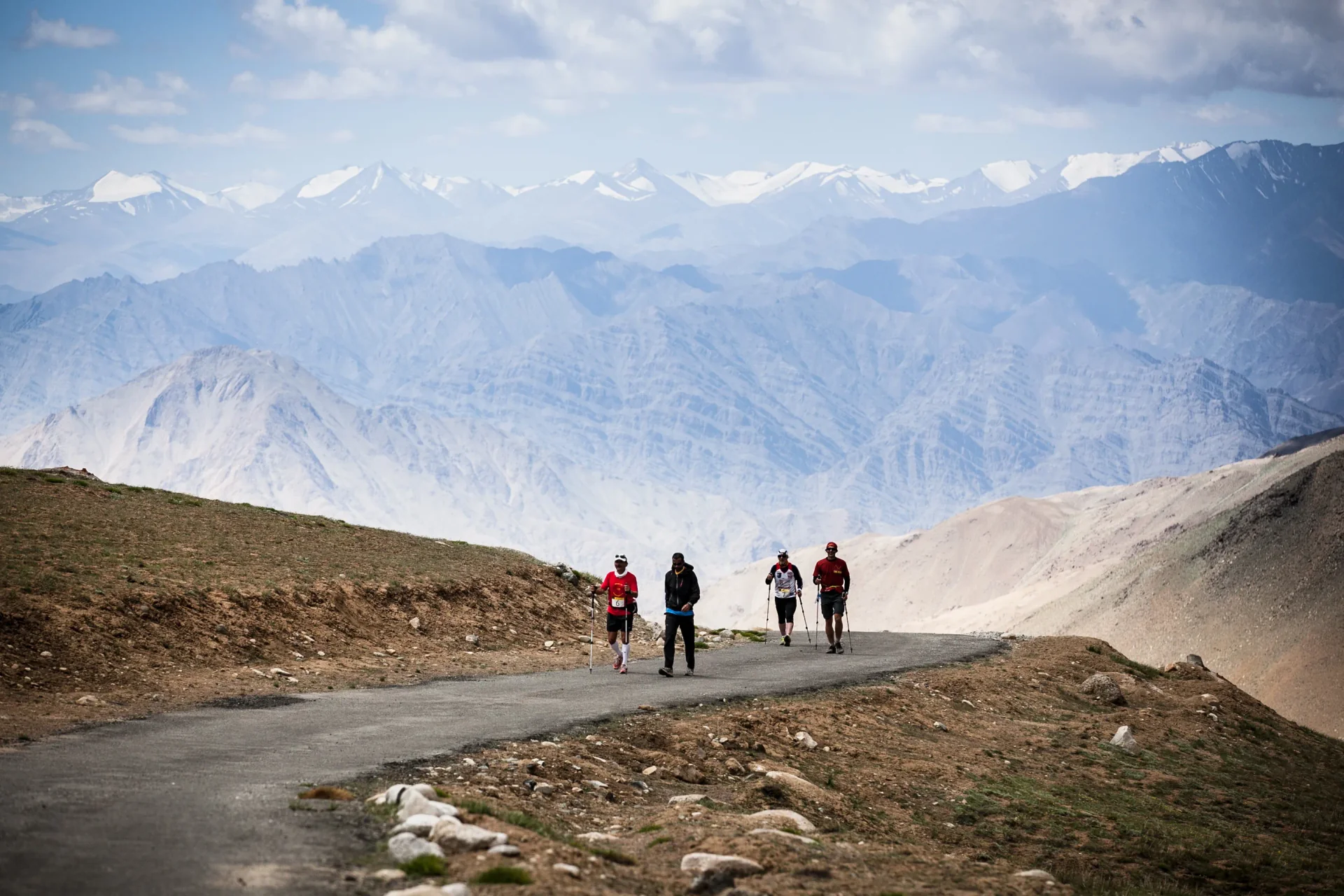 La Ultra runners on a winding mountain road beneath the vast mountains of Ladakh